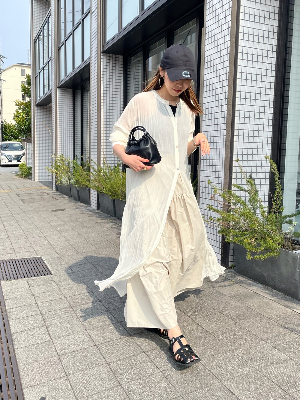 ブラック系のハンドバッグ、ホワイト系のワンピース、ブラック系のサンダルを着用したレディースの夏コーディネートの5枚目の写真