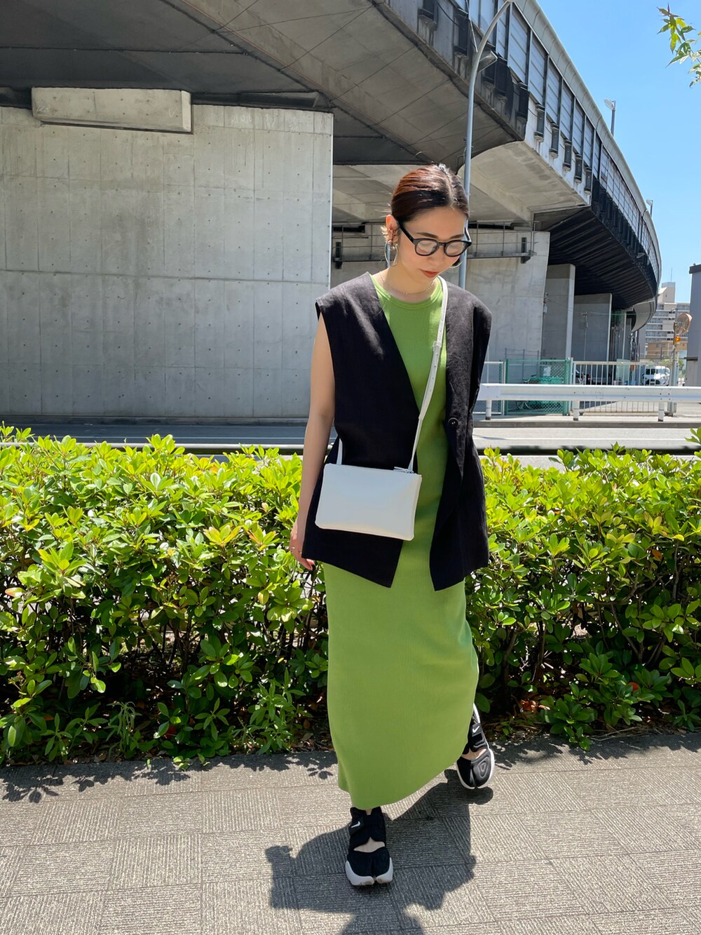 グリーン系のワンピース、ブラック系のベスト、ブラック系のスニーカーを着用したレディースの夏コーディネートの3枚目の写真