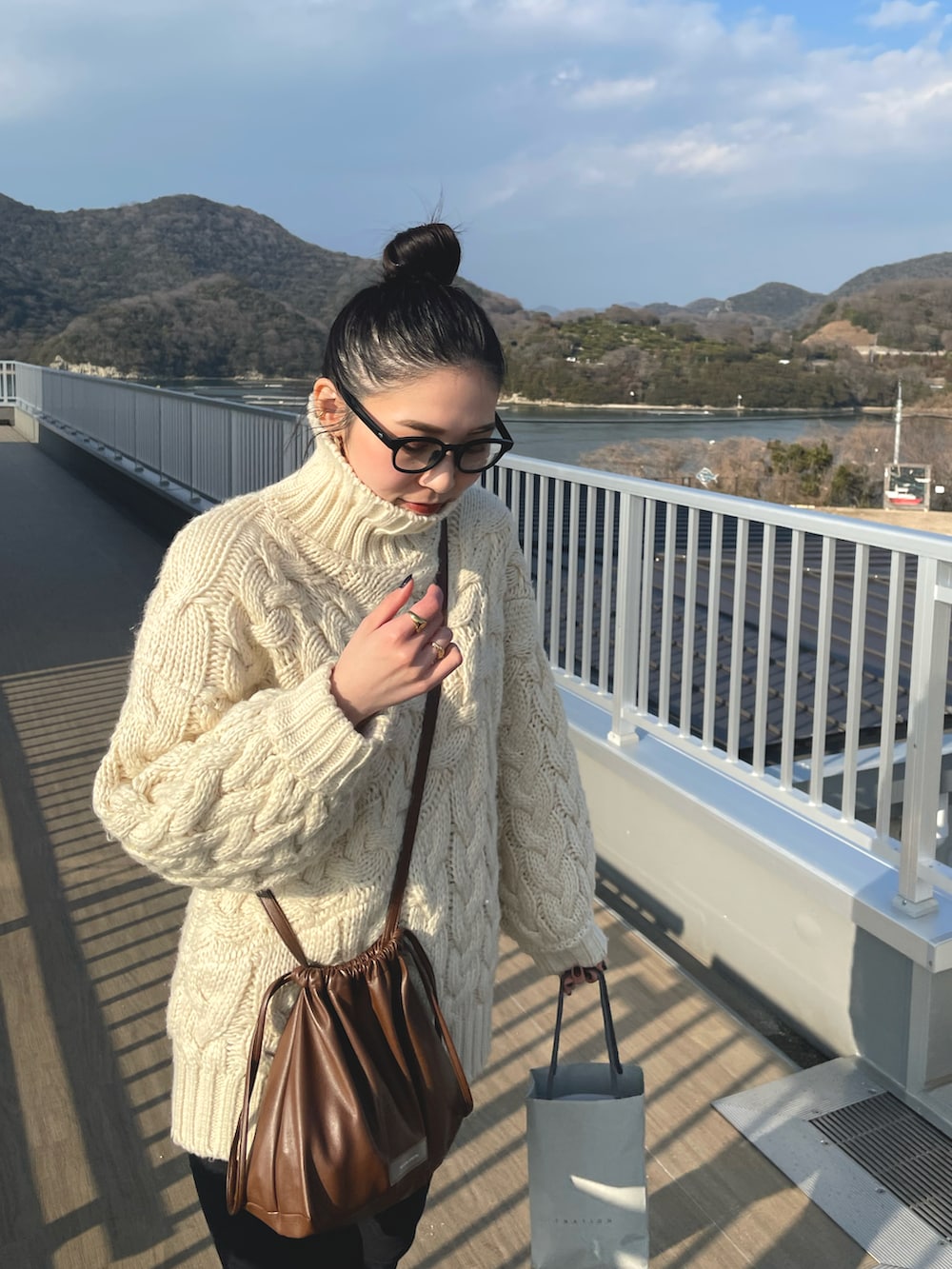 ブラウン系のショルダーバッグ、ブラック系のデニムパンツ、ブラック系のブーツを着用したレディースの冬コーディネートの4枚目の写真