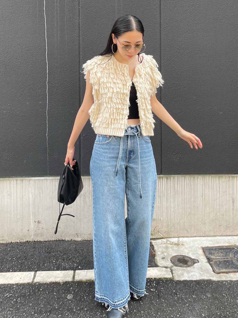 ブルー系のデニムパンツ、ホワイト系のベスト、ブラック系のショルダーバッグを着用したレディースの秋コーディネートの4枚目の写真