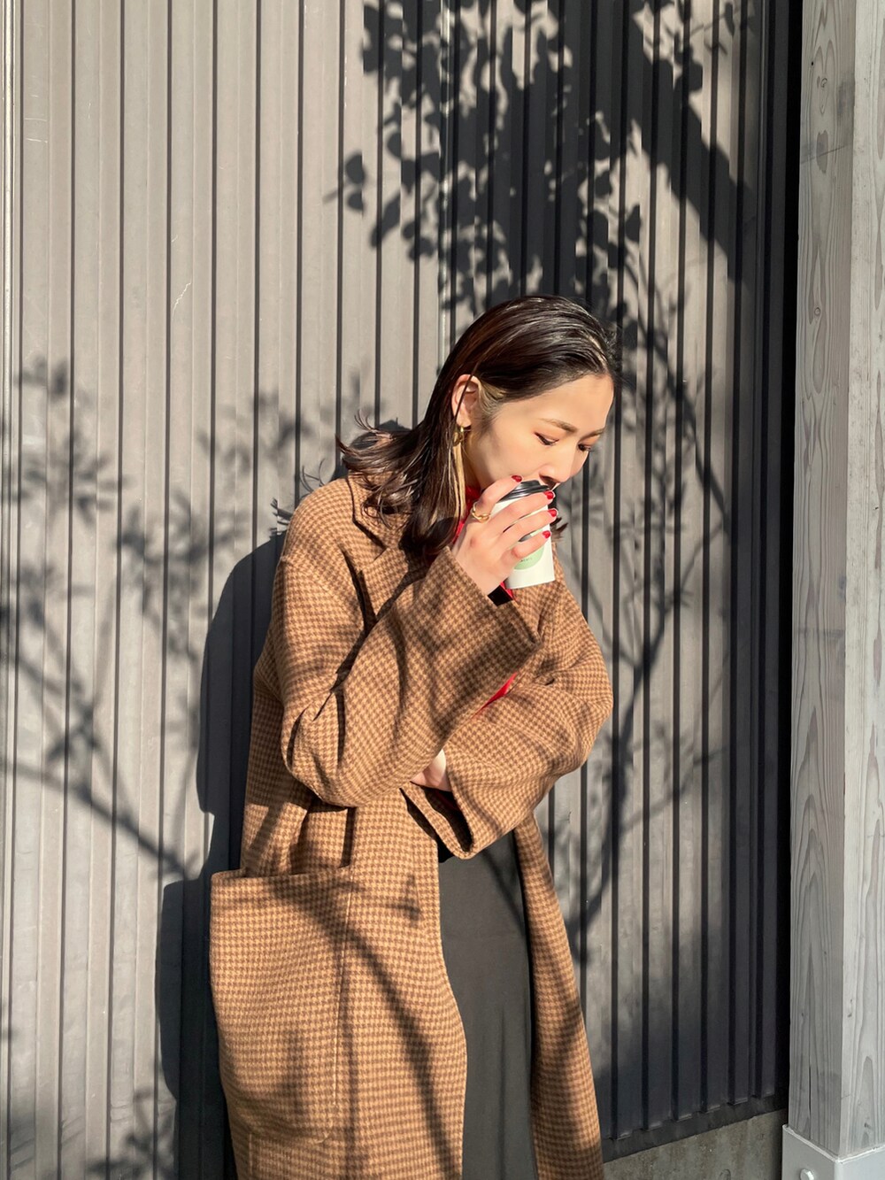 レッド系のニット/セーター、ブラウン系のチェスターコート、ブラック系のスカートを着用したレディースの冬コーディネートの3枚目の写真