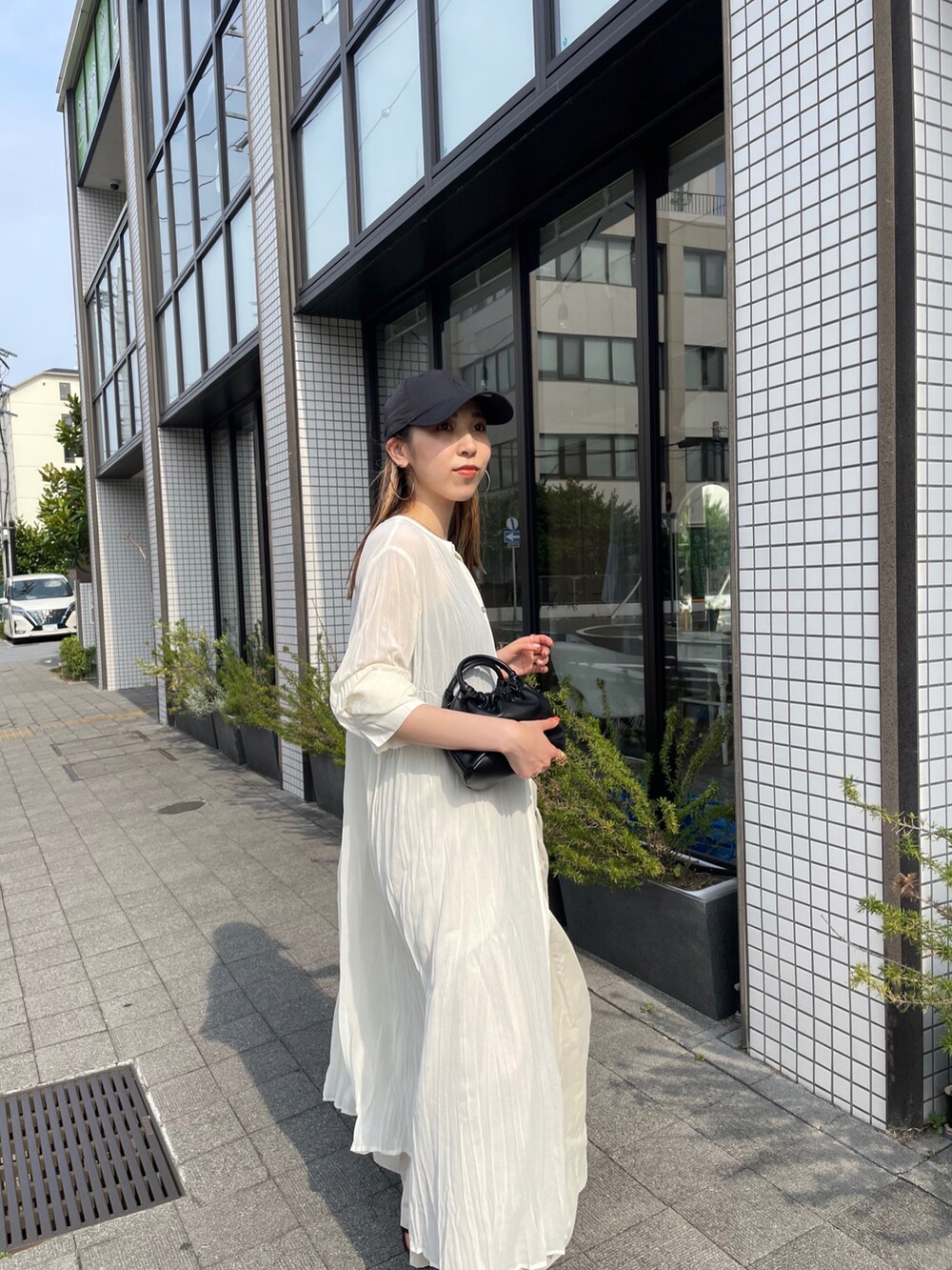 ブラック系のハンドバッグ、ホワイト系のワンピース、ブラック系のサンダルを着用したレディースの夏コーディネートの3枚目の写真