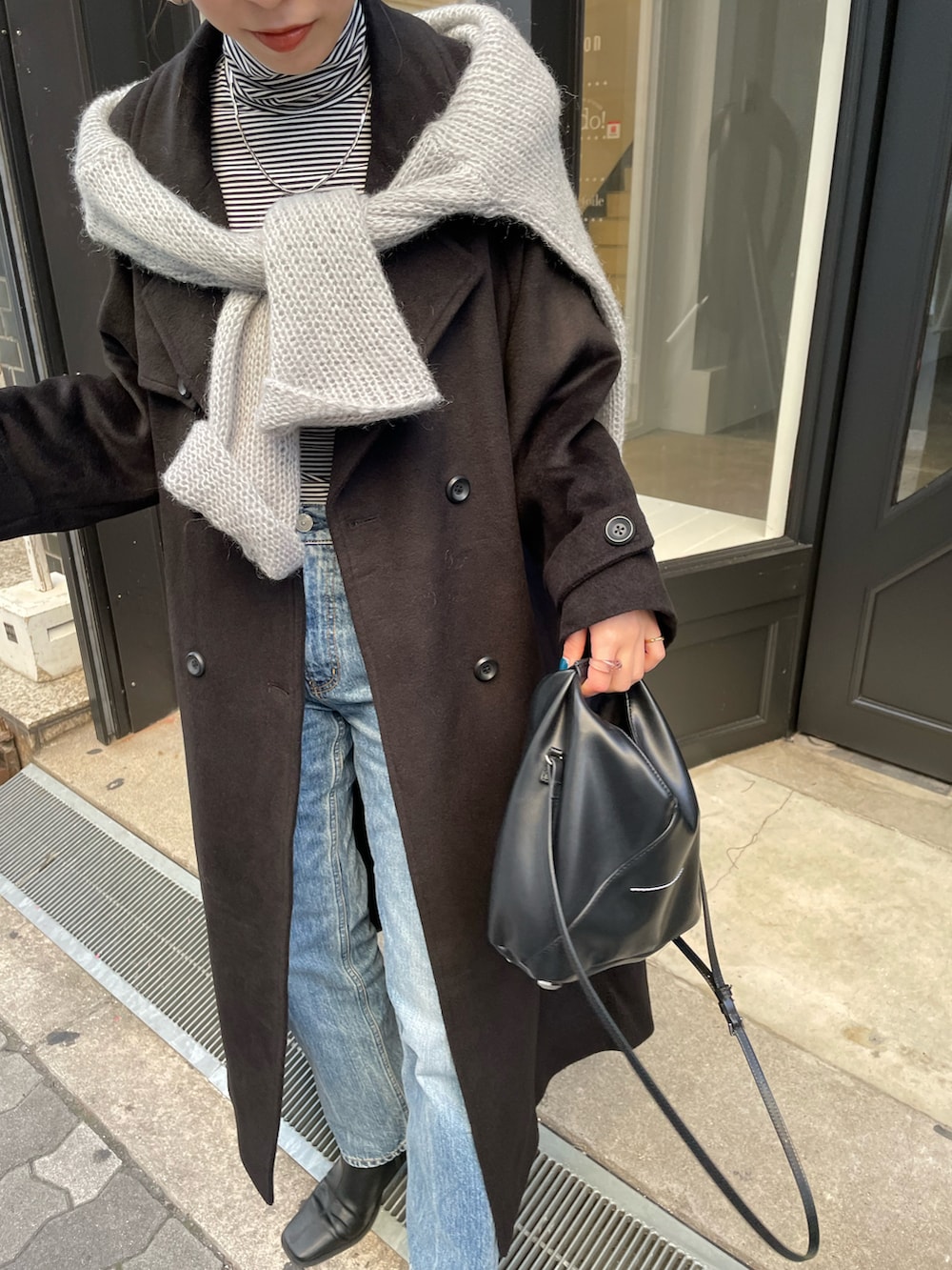 ブルー系のデニムパンツ、ブラック系のブーツ、ブラック系のチェスターコートを着用したレディースの秋コーディネートの5枚目の写真