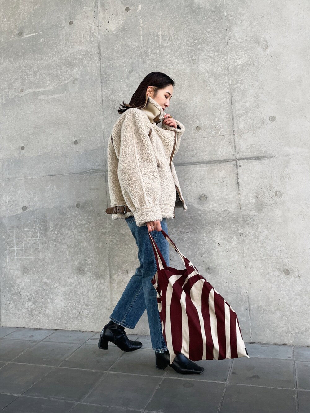 ホワイト系のブルゾン、ブルー系のデニムパンツ、レッド系のトートバッグを着用したレディースの冬コーディネートの2枚目の写真