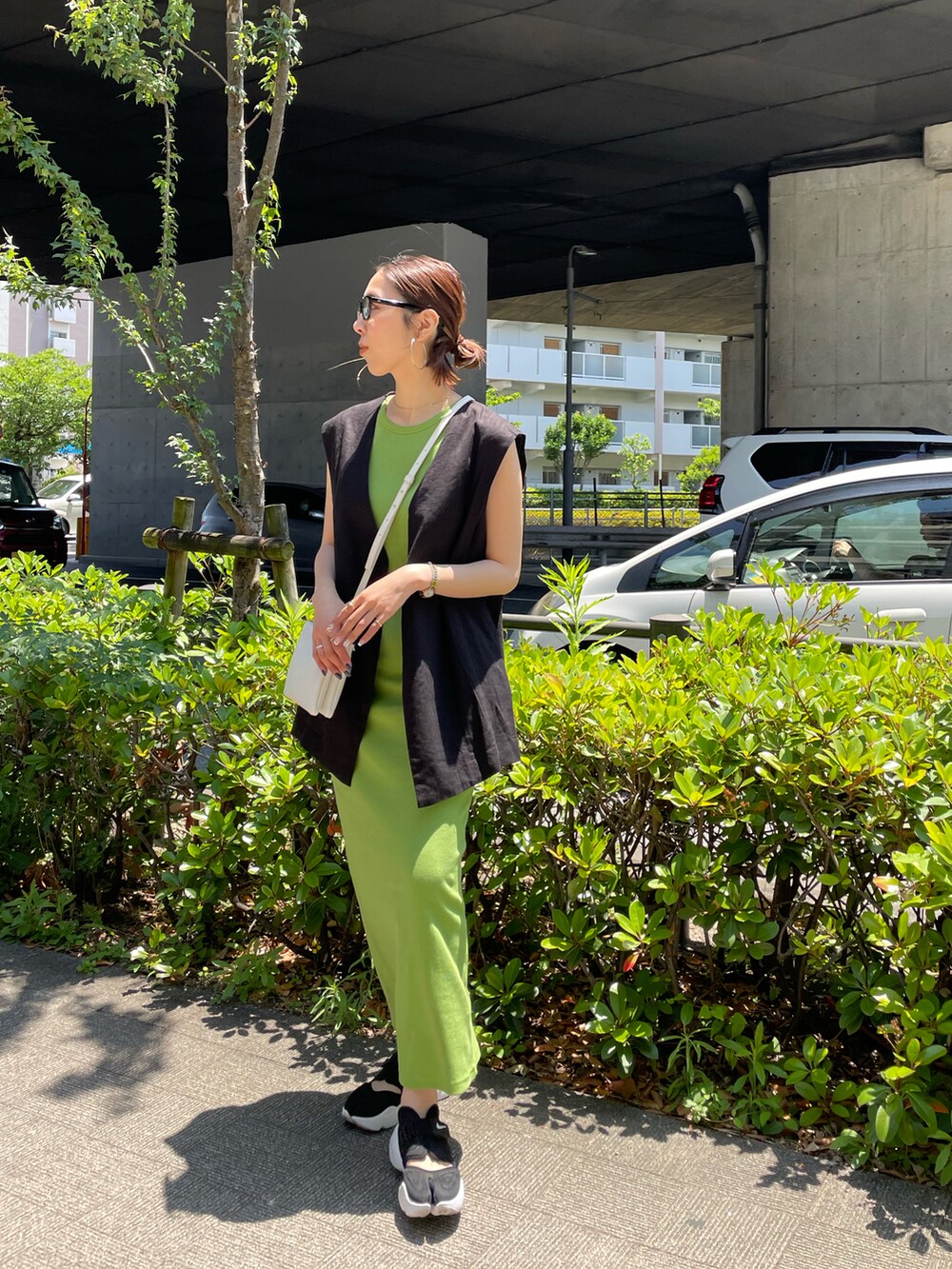 グリーン系のワンピース、ブラック系のベスト、ブラック系のスニーカーを着用したレディースの夏コーディネートの2枚目の写真