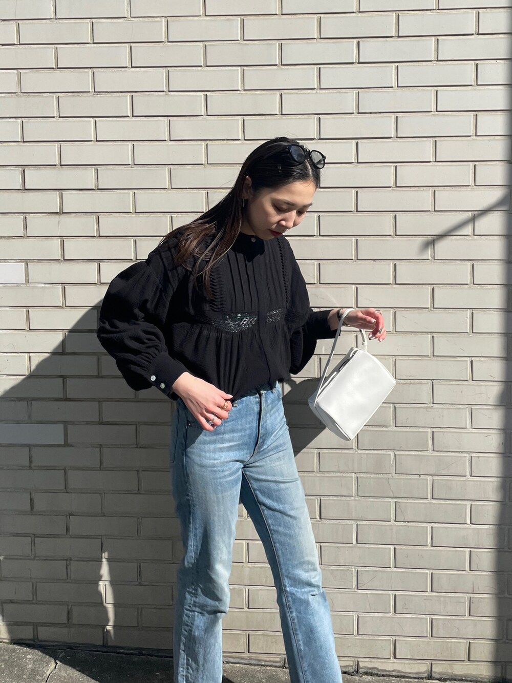 ブルー系のデニムパンツ、ホワイト系のハンドバッグ、ブラック系のシャツ/ブラウスを着用したレディースの冬コーディネートの4枚目の写真