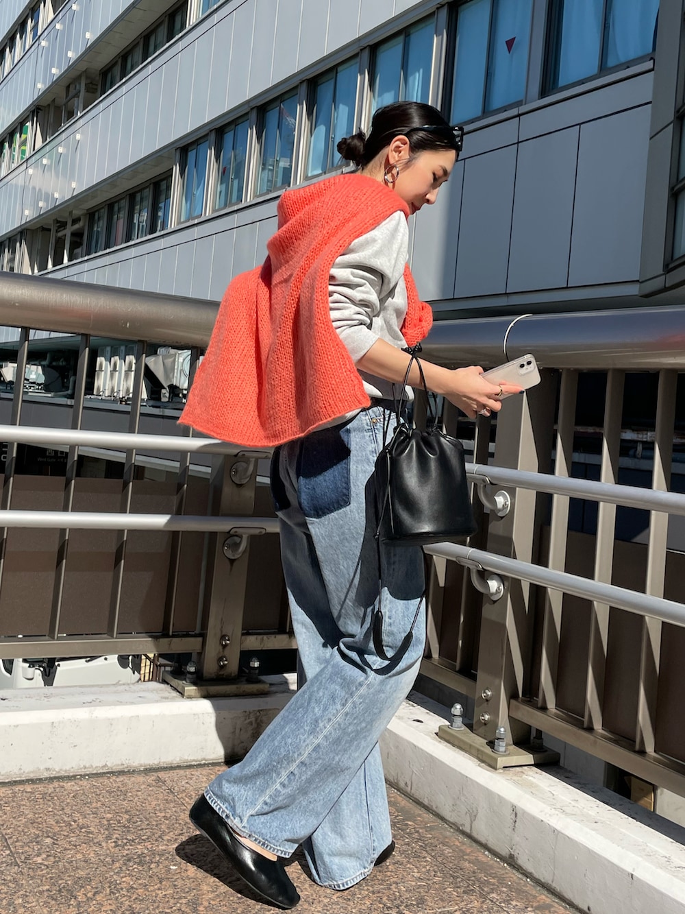 ブラック系のハンドバッグ、オレンジ系のニット/セーター、ブルー系のデニムパンツを着用したレディースの秋コーディネートの3枚目の写真
