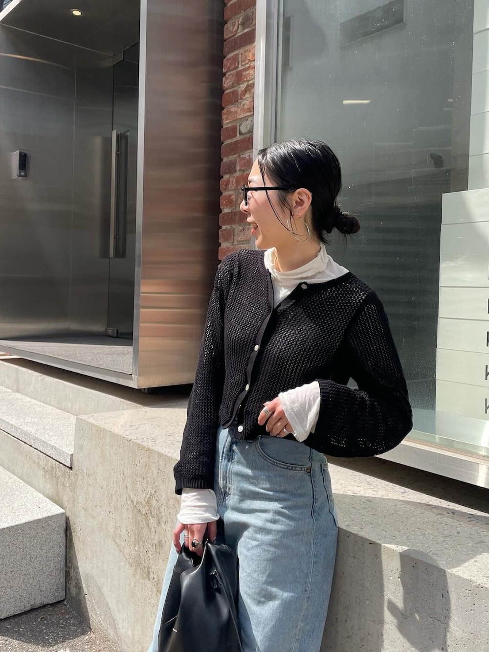 ブルー系のデニムパンツ、ブラック系のカーディガン/ボレロ、ブラック系のショルダーバッグを着用したレディースの春コーディネートの5枚目の写真