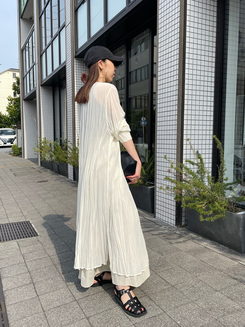 ブラック系のハンドバッグ、ホワイト系のワンピース、ブラック系のサンダルを着用したレディースの夏コーディネートの4枚目の写真