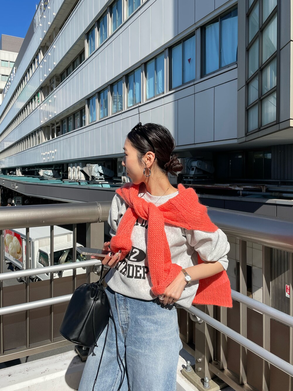 ブラック系のハンドバッグ、オレンジ系のニット/セーター、ブルー系のデニムパンツを着用したレディースの秋コーディネートの4枚目の写真