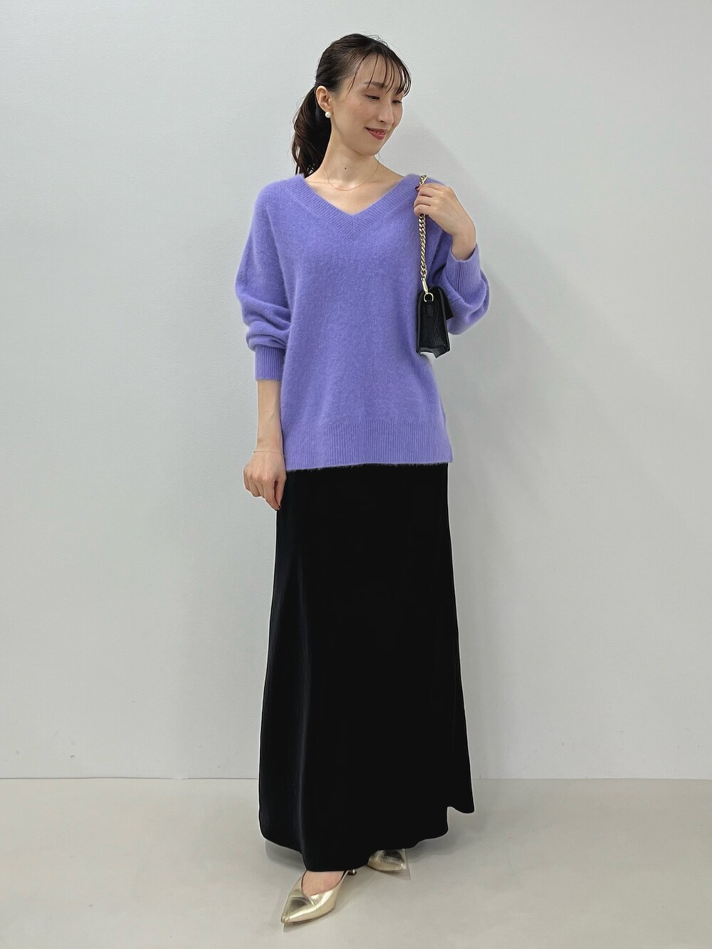 パープル系のニット/セーター、ゴールド系のショルダーバッグ、ブラック系のスカートを着用したレディースの秋コーディネートの5枚目の写真