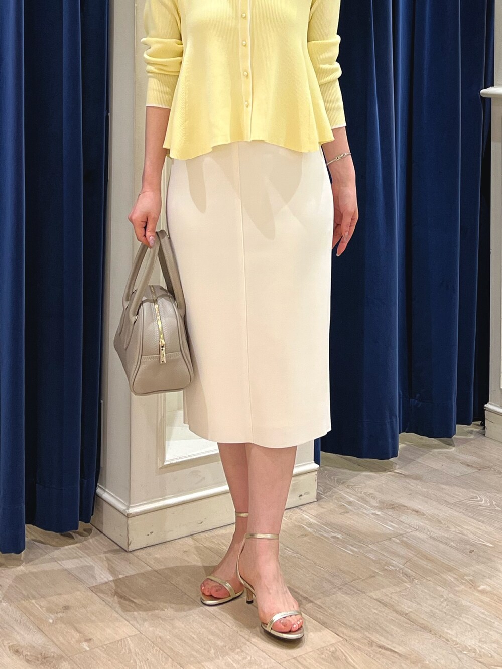 ベージュ系のカーディガン/ボレロ、ホワイト系のスカート、ベージュ系のボストンバッグを着用したレディースの春コーディネートの6枚目の写真