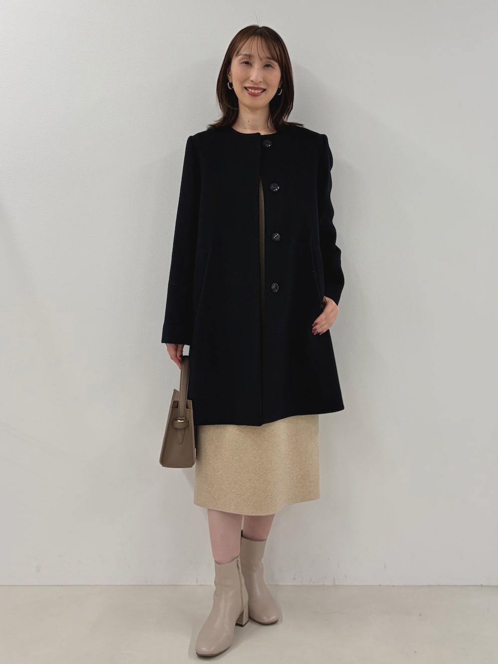 ブルー系のノーカラーコート、ベージュ系のワンピース、ベージュ系のショルダーバッグを着用したレディースの秋コーディネートの4枚目の写真