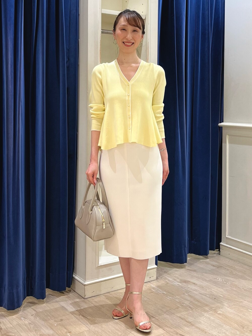 ベージュ系のカーディガン/ボレロ、ホワイト系のスカート、ベージュ系のボストンバッグを着用したレディースの春コーディネートの8枚目の写真