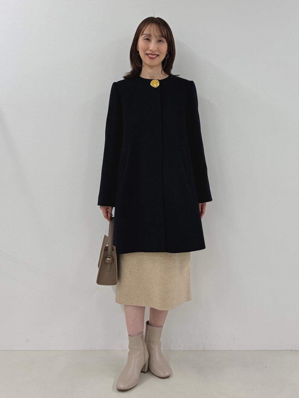 ブルー系のノーカラーコート、ベージュ系のワンピース、ベージュ系のショルダーバッグを着用したレディースの秋コーディネートの6枚目の写真