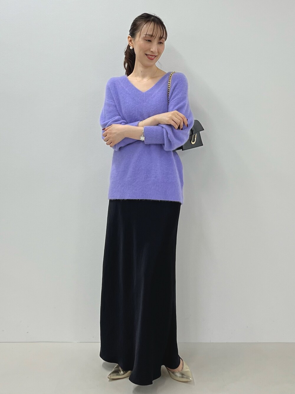 パープル系のニット/セーター、ゴールド系のショルダーバッグ、ブラック系のスカートを着用したレディースの秋コーディネートの6枚目の写真