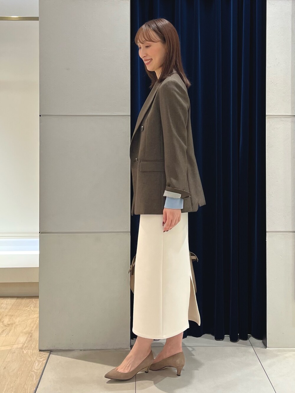 ブラウン系のテーラードジャケット、ブルー系のニット/セーター、ホワイト系のスカートを着用したレディースの秋コーディネートの6枚目の写真