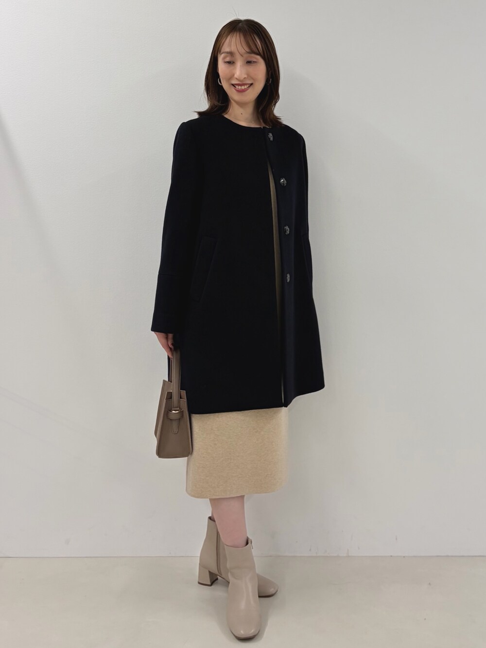 ブルー系のノーカラーコート、ベージュ系のワンピース、ベージュ系のショルダーバッグを着用したレディースの秋コーディネートの9枚目の写真