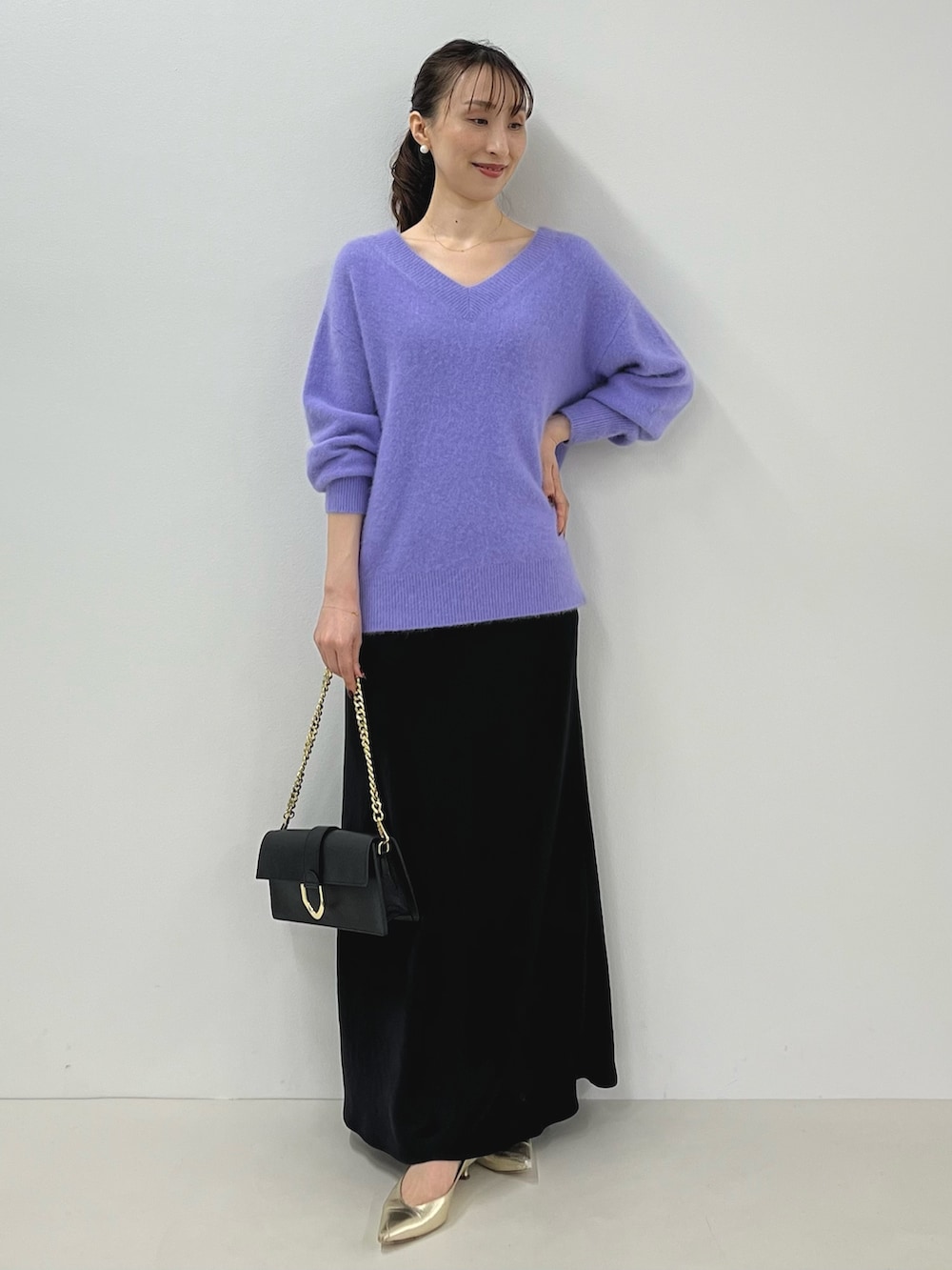 パープル系のニット/セーター、ゴールド系のショルダーバッグ、ブラック系のスカートを着用したレディースの秋コーディネートの2枚目の写真