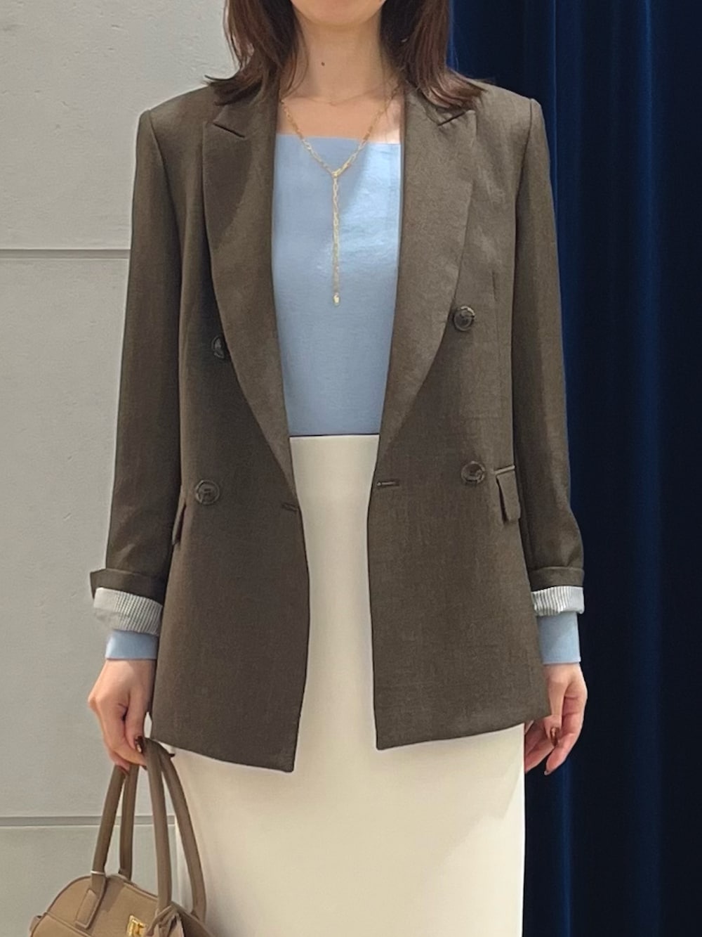 ブラウン系のテーラードジャケット、ブルー系のニット/セーター、ホワイト系のスカートを着用したレディースの秋コーディネートの3枚目の写真
