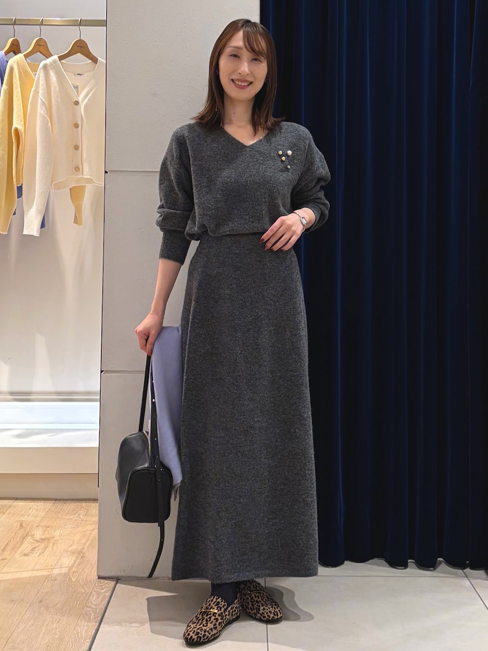 グレー系のニット/セーター、グレー系のスカート、ブラック系のショルダーバッグを着用したレディースの冬コーディネートの2枚目の写真