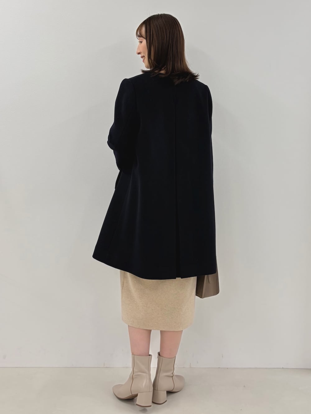 ブルー系のノーカラーコート、ベージュ系のワンピース、ベージュ系のショルダーバッグを着用したレディースの秋コーディネートの8枚目の写真