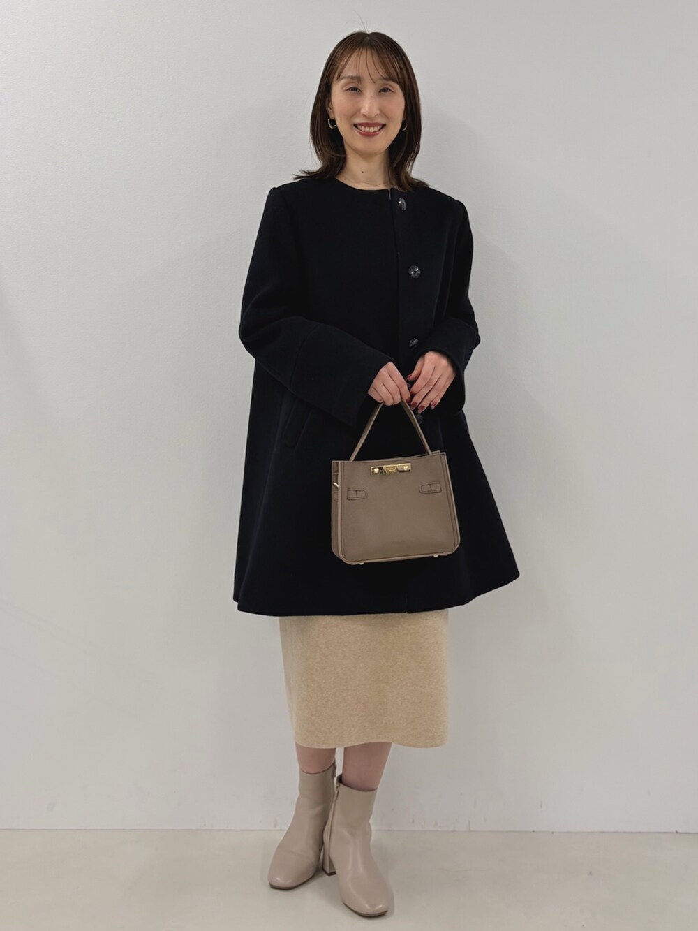 ブルー系のノーカラーコート、ベージュ系のワンピース、ベージュ系のショルダーバッグを着用したレディースの秋コーディネートの7枚目の写真