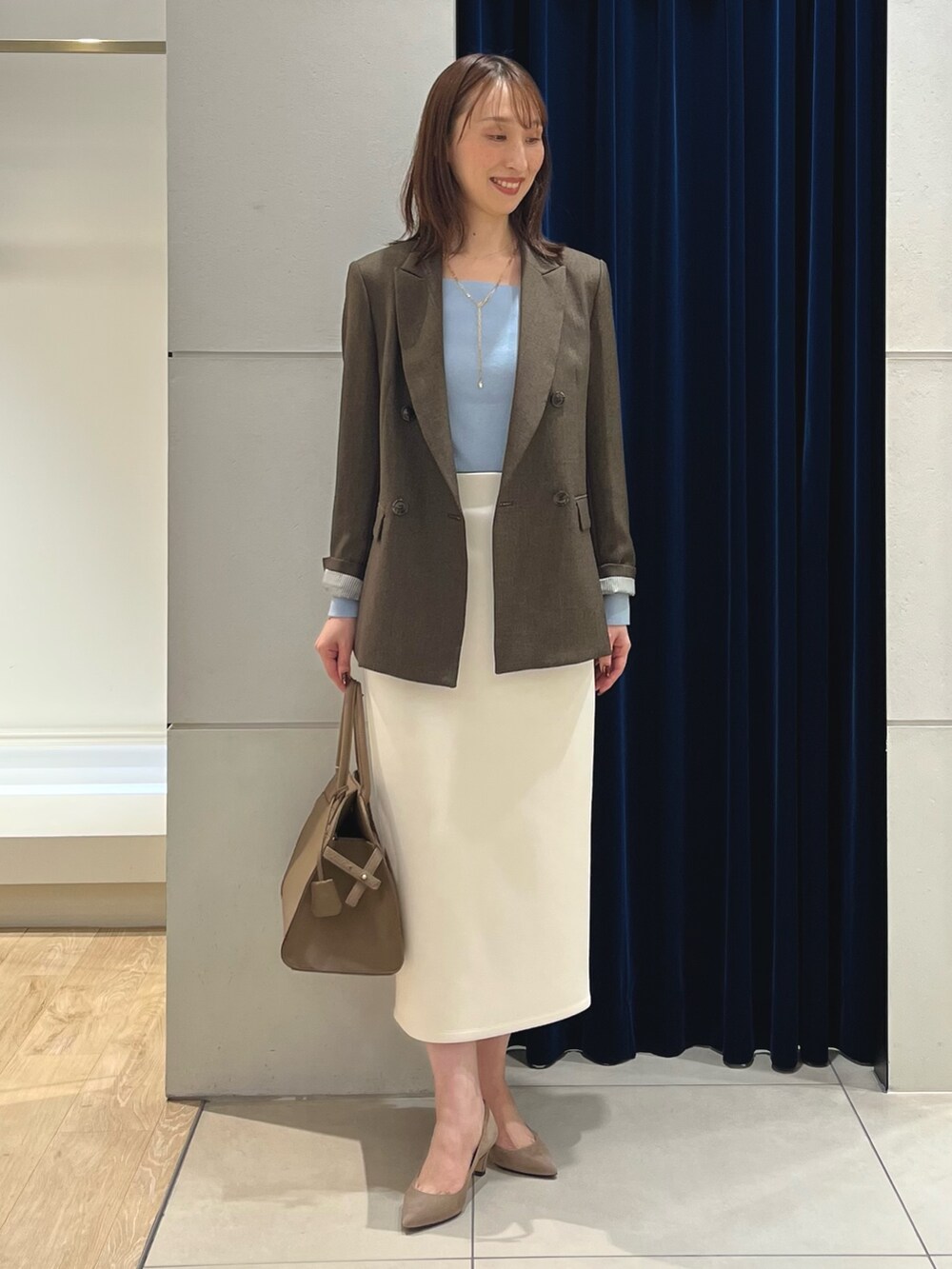 ブラウン系のテーラードジャケット、ブルー系のニット/セーター、ホワイト系のスカートを着用したレディースの秋コーディネートの7枚目の写真