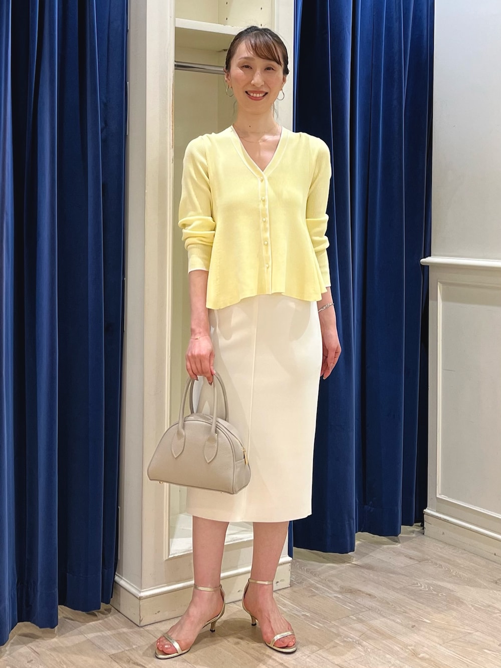 ベージュ系のカーディガン/ボレロ、ホワイト系のスカート、ベージュ系のボストンバッグを着用したレディースの春コーディネートの2枚目の写真