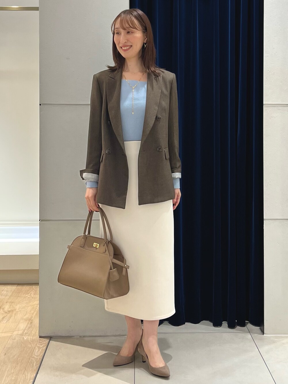 ブラウン系のテーラードジャケット、ブルー系のニット/セーター、ホワイト系のスカートを着用したレディースの秋コーディネートの2枚目の写真