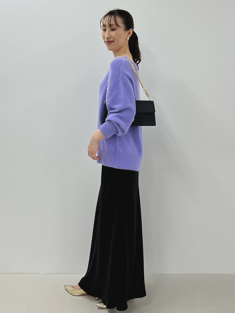 パープル系のニット/セーター、ゴールド系のショルダーバッグ、ブラック系のスカートを着用したレディースの秋コーディネートの8枚目の写真