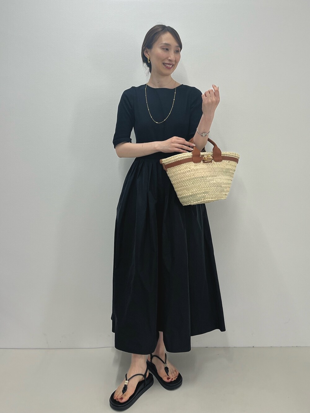 ブラック系のワンピース、ブラウン系のかごバッグ、ブラック系のサンダルを着用したレディースの春コーディネートの7枚目の写真