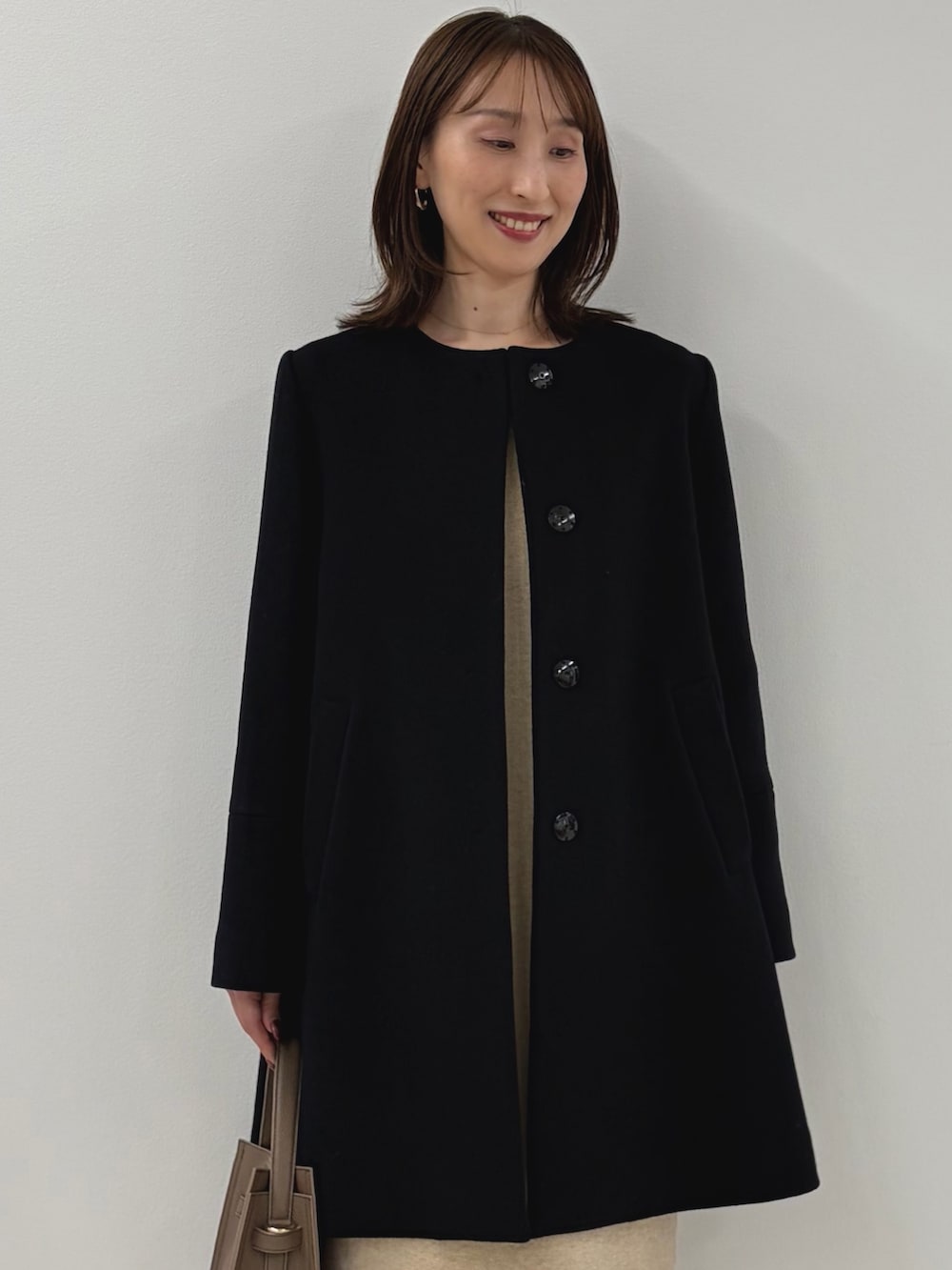 ブルー系のノーカラーコート、ベージュ系のワンピース、ベージュ系のショルダーバッグを着用したレディースの秋コーディネートの3枚目の写真