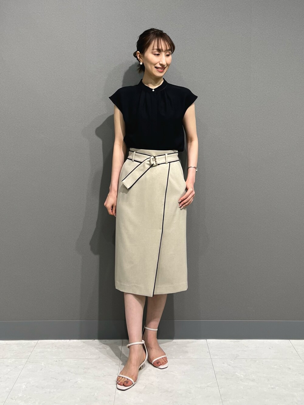 ブラック系のシャツ/ブラウス、ベージュ系のスカート、ホワイト系のサンダルを着用したレディースの春コーディネートの2枚目の写真