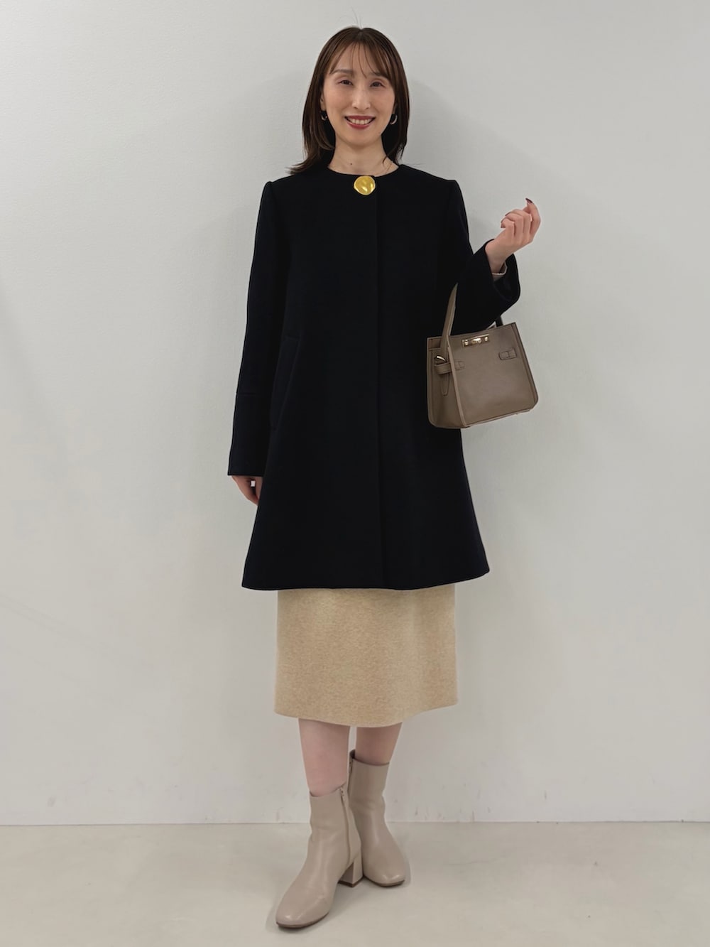 ブルー系のノーカラーコート、ベージュ系のワンピース、ベージュ系のショルダーバッグを着用したレディースの秋コーディネートの2枚目の写真