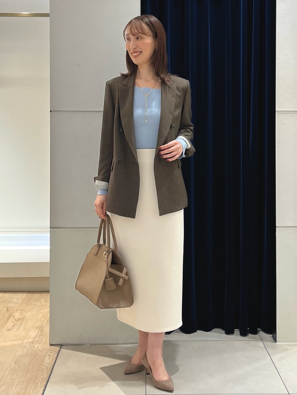 ブラウン系のテーラードジャケット、ブルー系のニット/セーター、ホワイト系のスカートを着用したレディースの秋コーディネートの5枚目の写真
