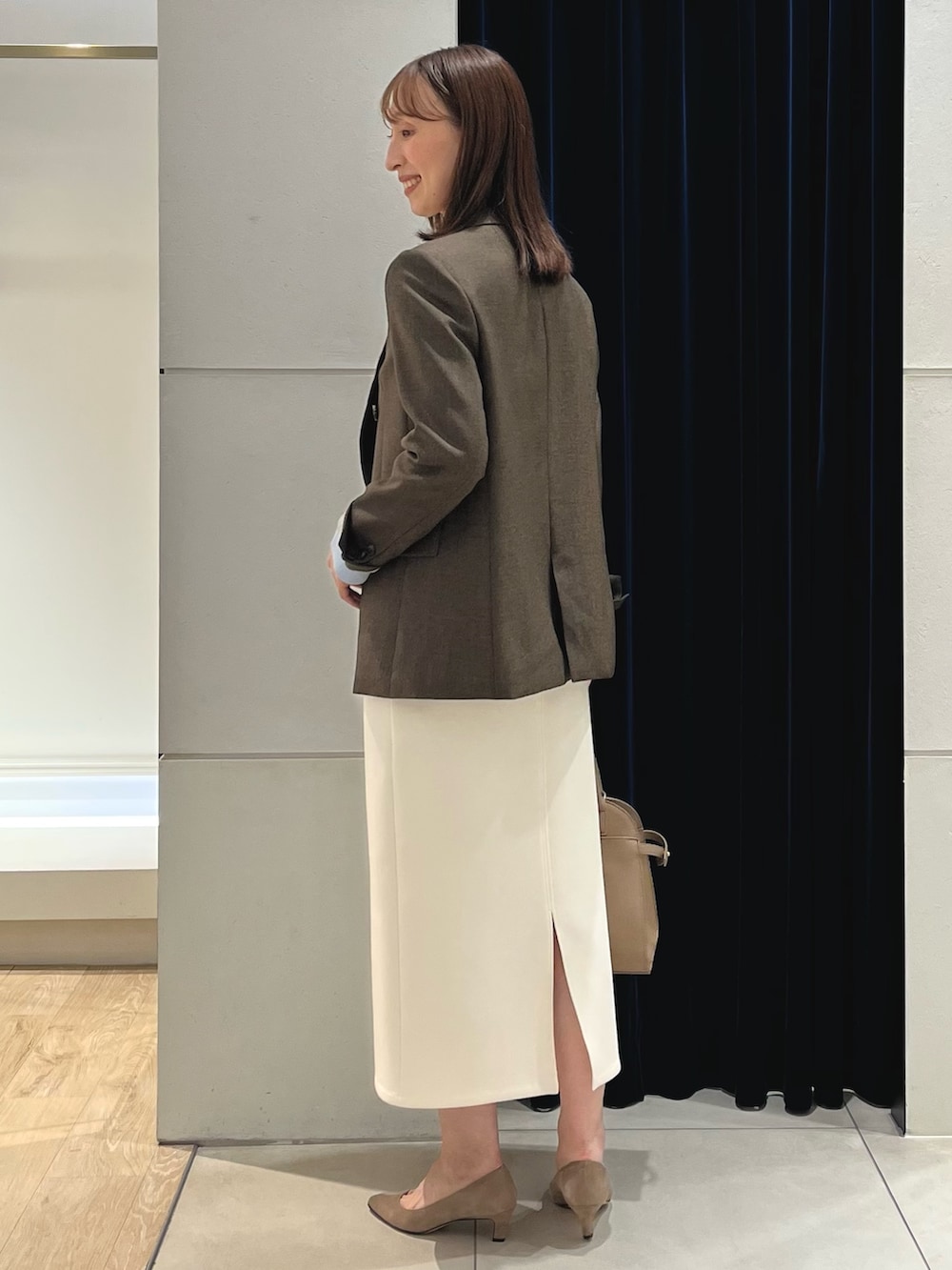 ブラウン系のテーラードジャケット、ブルー系のニット/セーター、ホワイト系のスカートを着用したレディースの秋コーディネートの9枚目の写真