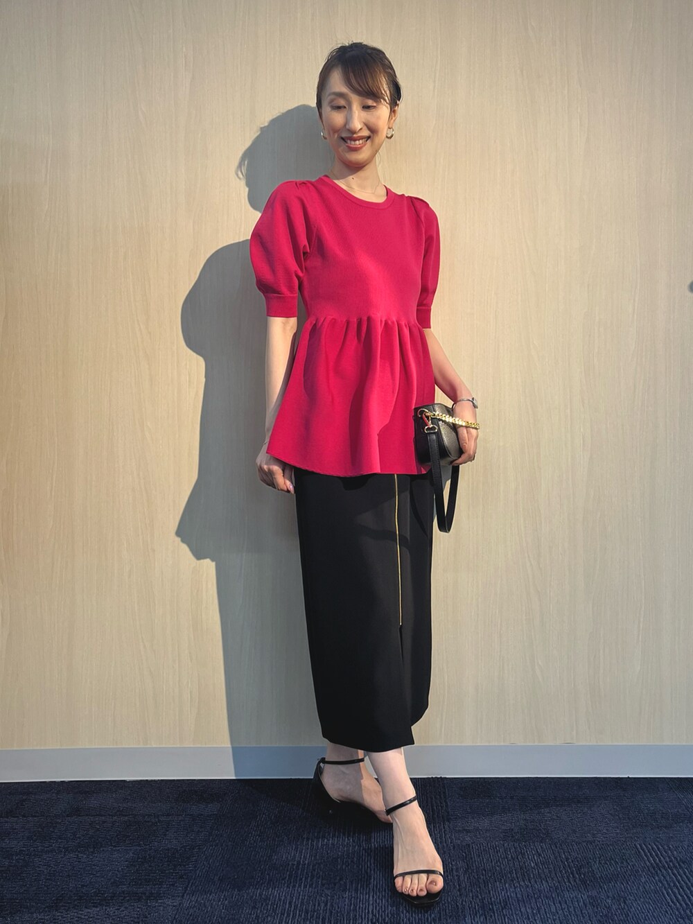 ピンク系のニット/セーター、ブラック系のショルダーバッグ、ブラック系のスカートを着用したレディースの夏コーディネートの2枚目の写真
