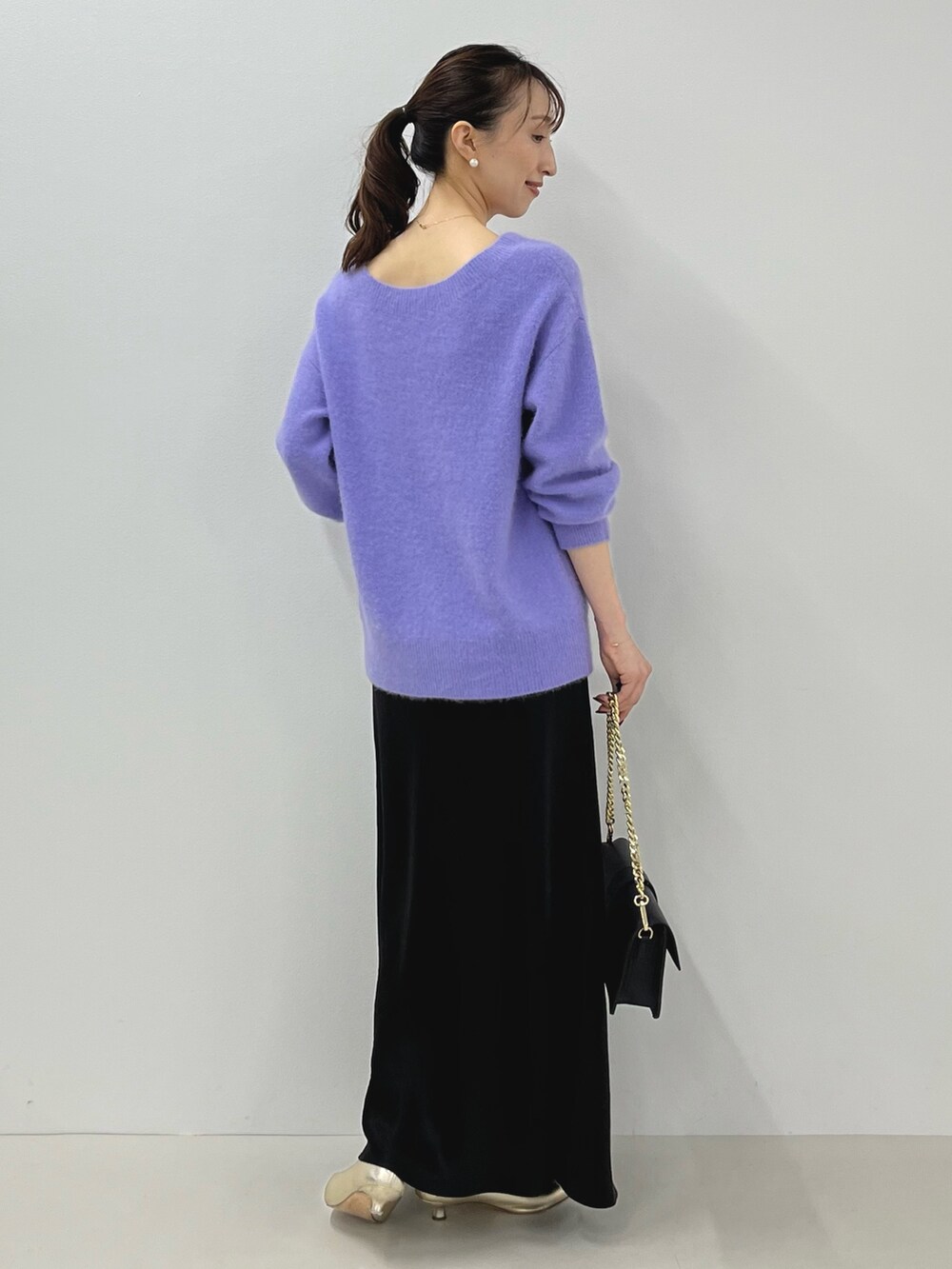 パープル系のニット/セーター、ゴールド系のショルダーバッグ、ブラック系のスカートを着用したレディースの秋コーディネートの9枚目の写真