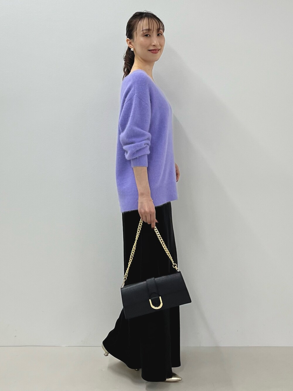 パープル系のニット/セーター、ゴールド系のショルダーバッグ、ブラック系のスカートを着用したレディースの秋コーディネートの10枚目の写真