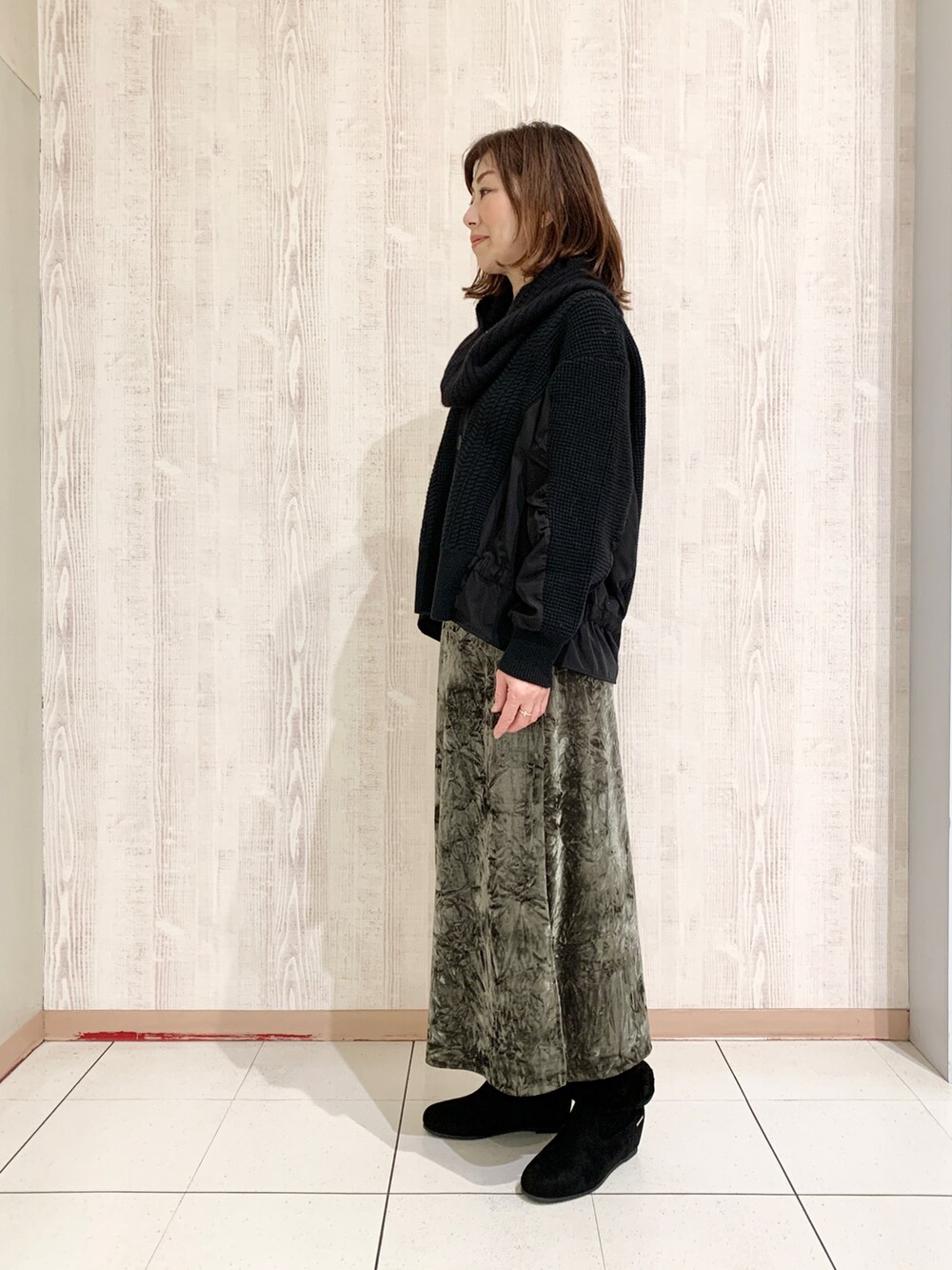 ブラック系のニット/セーター、グリーン系のスカート、ブラック系のブーツを着用したレディースの秋コーディネートの2枚目の写真