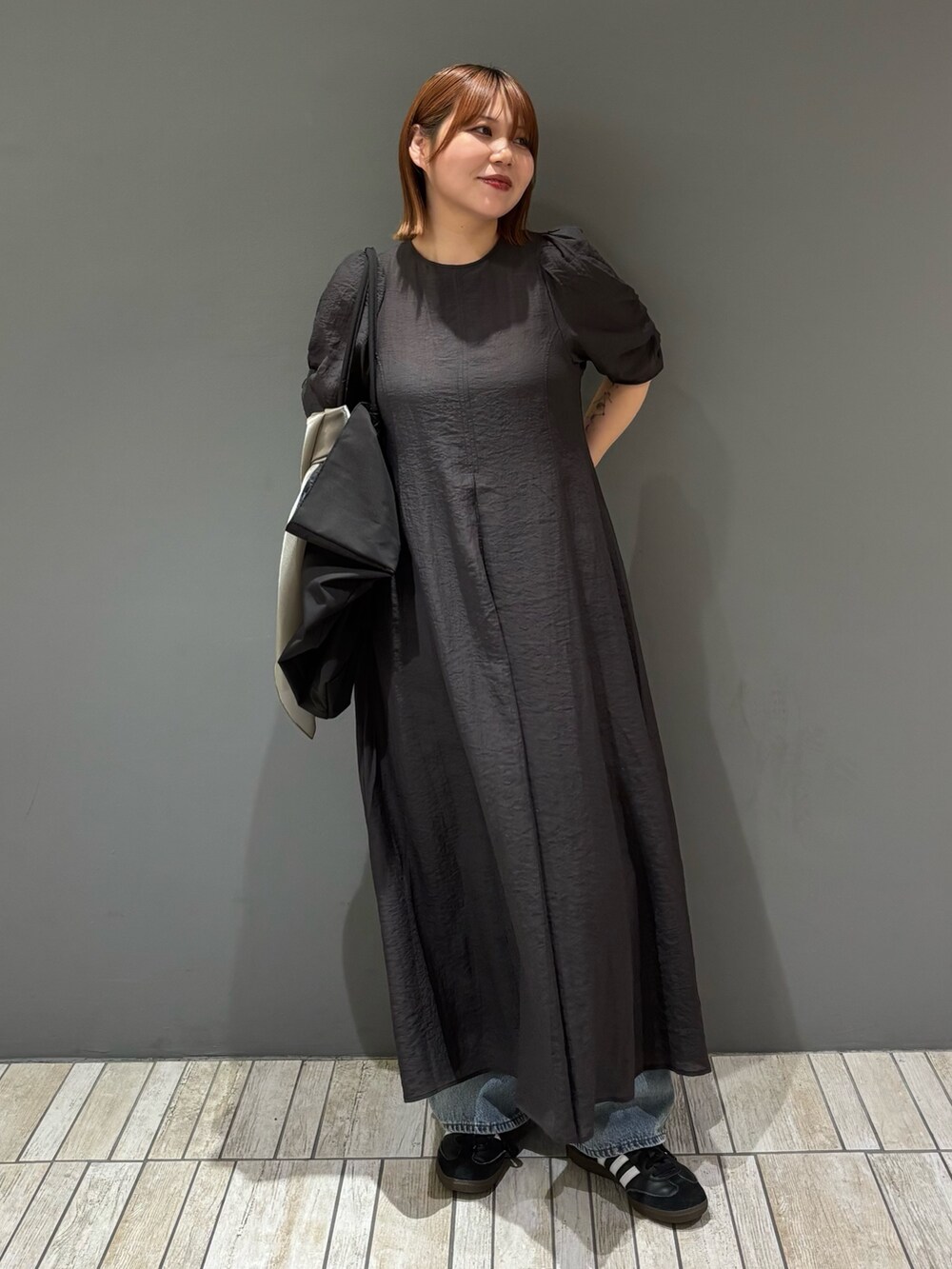 ブラック系のショルダーバッグ、ブルー系のデニムパンツ、グレー系のワンピースを着用したレディースの春コーディネートの2枚目の写真