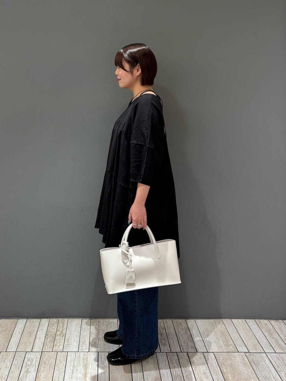 ブラック系のワンピース、ホワイト系のハンドバッグ、ブルー系のデニムパンツを着用したレディースの春コーディネートの3枚目の写真