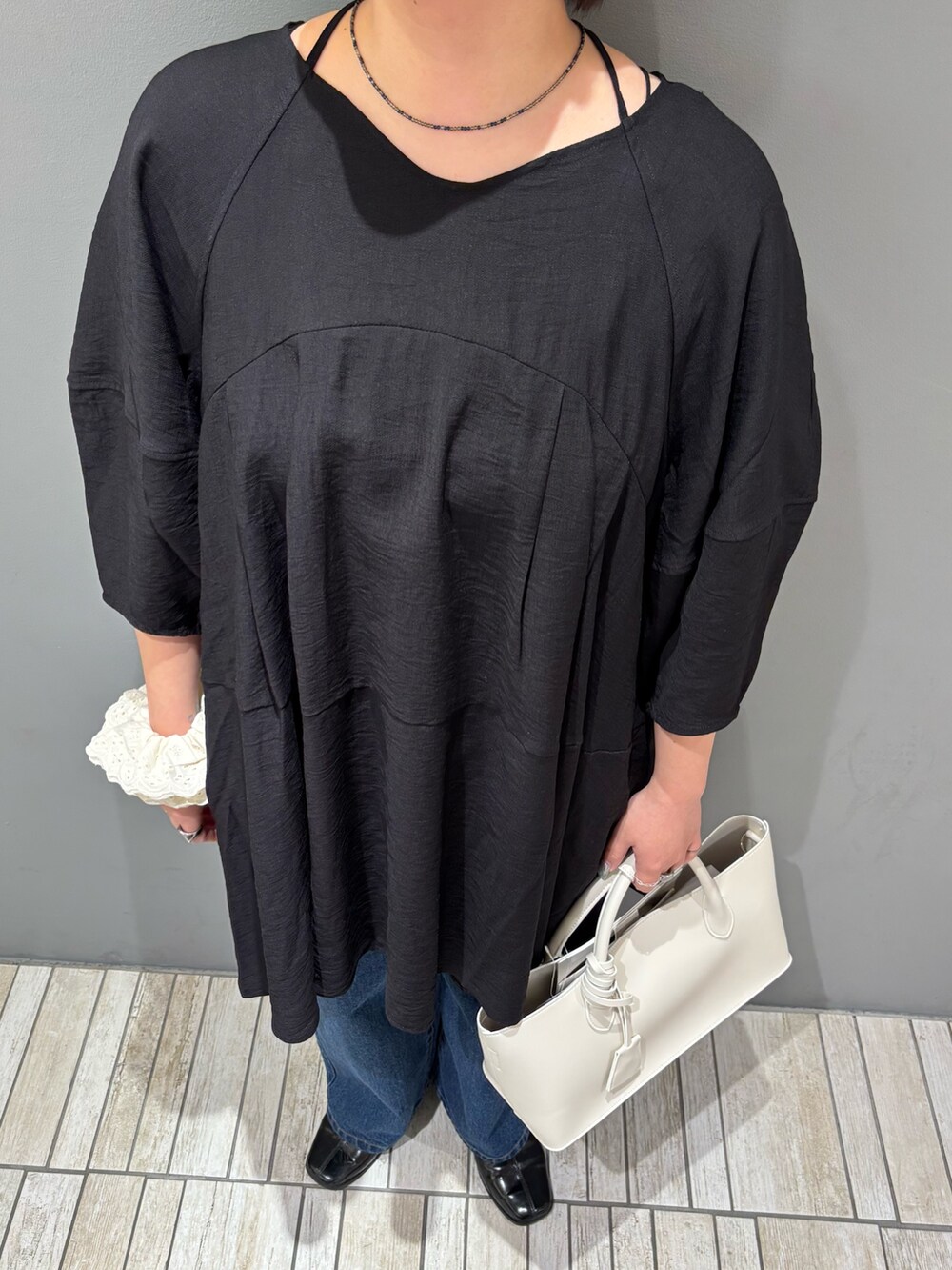 ブラック系のワンピース、ホワイト系のハンドバッグ、ブルー系のデニムパンツを着用したレディースの春コーディネートの6枚目の写真