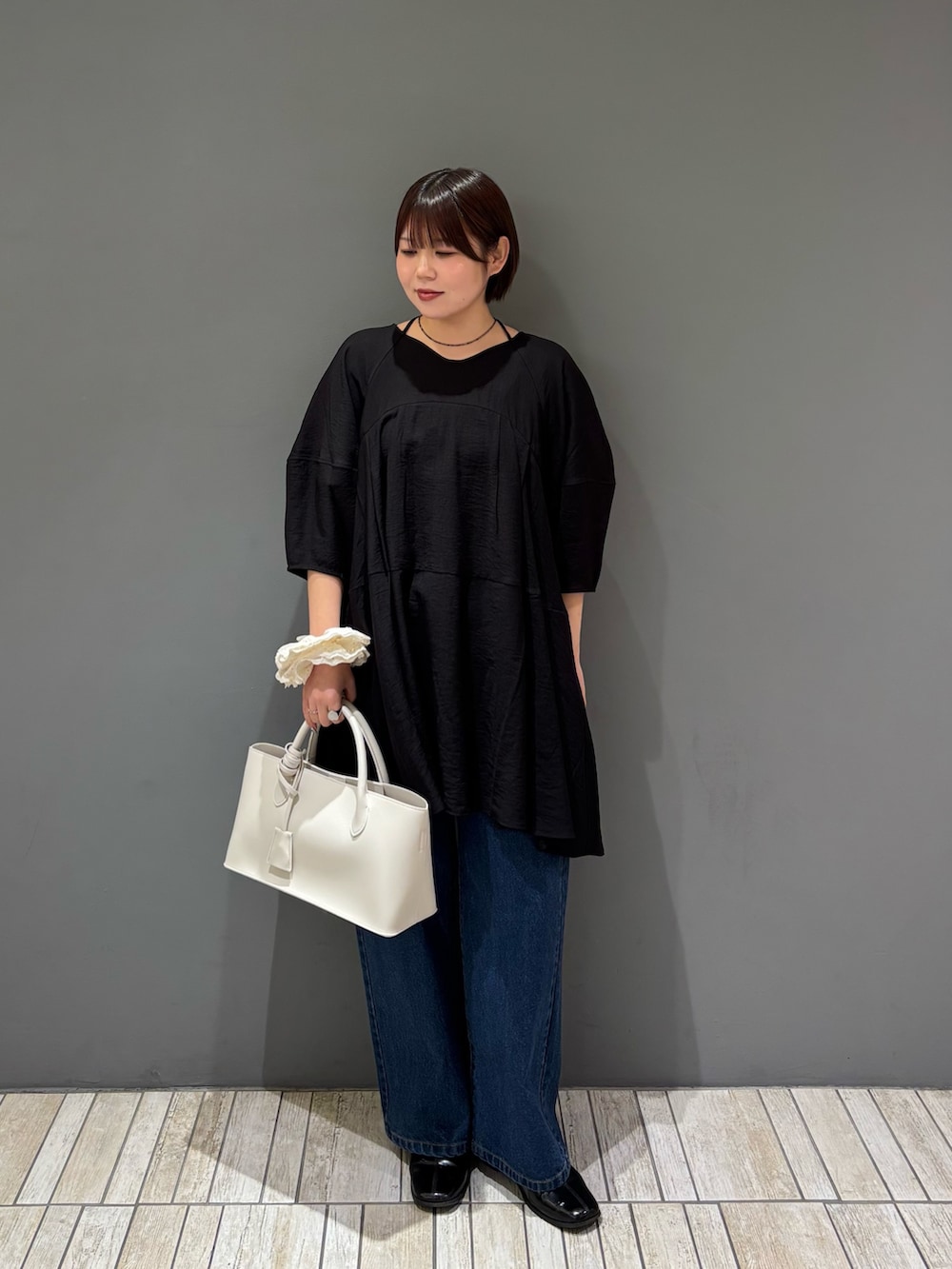 ブラック系のワンピース、ホワイト系のハンドバッグ、ブルー系のデニムパンツを着用したレディースの春コーディネートの2枚目の写真