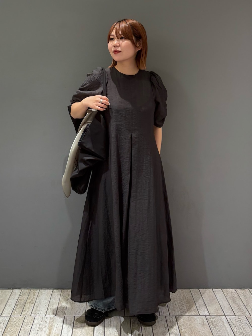 ブラック系のショルダーバッグ、ブルー系のデニムパンツ、グレー系のワンピースを着用したレディースの春コーディネートの5枚目の写真