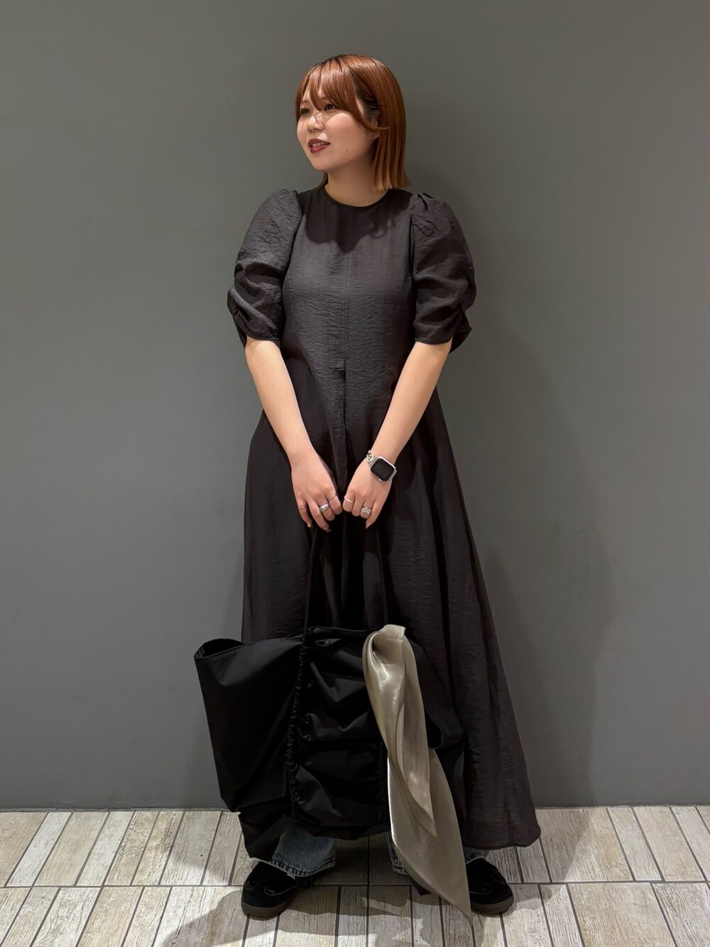 ブラック系のショルダーバッグ、ブルー系のデニムパンツ、グレー系のワンピースを着用したレディースの春コーディネートの3枚目の写真