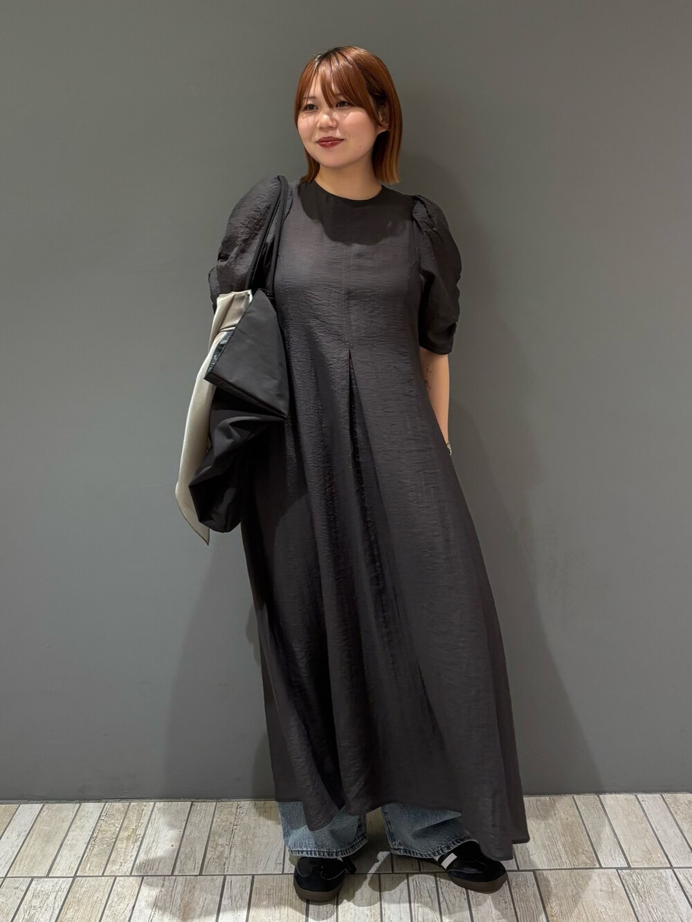 ブラック系のショルダーバッグ、ブルー系のデニムパンツ、グレー系のワンピースを着用したレディースの春コーディネートの4枚目の写真