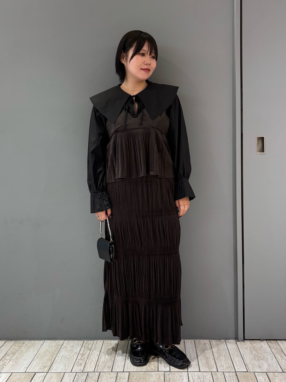 ブラック系のシャツ/ブラウス、ブラウン系のワンピース、ブラック系のローファーを着用したレディースの秋コーディネートの2枚目の写真