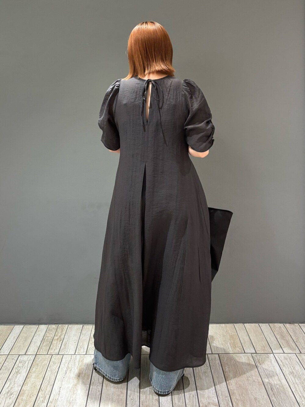 ブラック系のショルダーバッグ、ブルー系のデニムパンツ、グレー系のワンピースを着用したレディースの春コーディネートの7枚目の写真